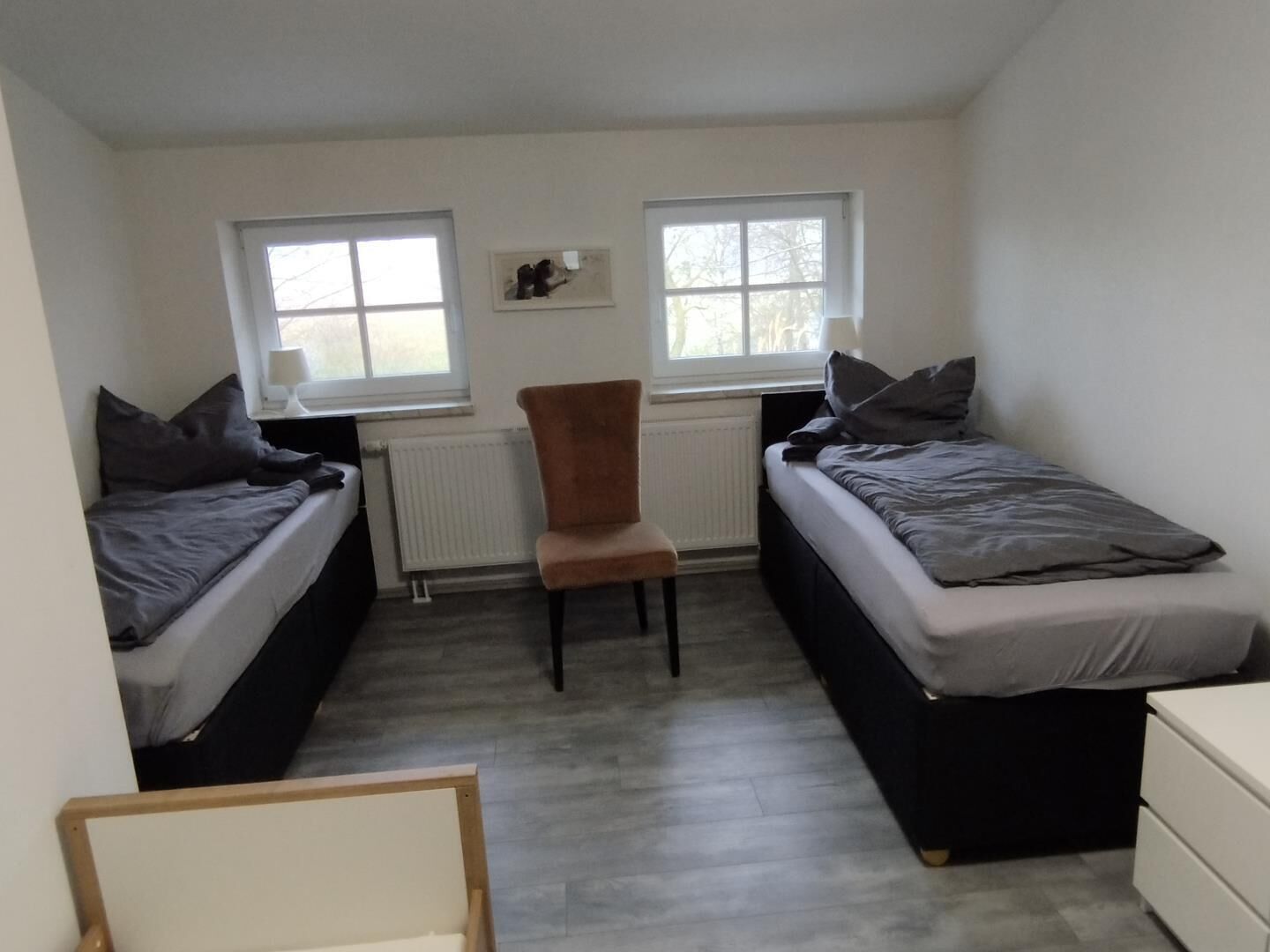 A small, compact room with two single beds, a chair, and a radiator.