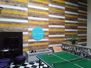 A hostel room with a checkered floor, a green ping pong table, a television, and a sign that reads "Casa Copada, Uruguay". - Casa Copada (Montevideo)