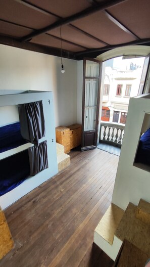 A room with two bunk beds, a wooden floor, a door leading outside, and a small wooden bench. - Casa Copada (Montevideo)