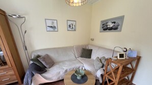 A cozy living room with a sofa, a small round table, and a wooden side table. - Der Zweckmäßig Ausgestattete Bungalow in Börgerende mit ca. 42 qm Wohnfläche Verfügt Über Eine gut Abgeschirmte Sonnenterrasse in Süd-/westlage (Börgerende)