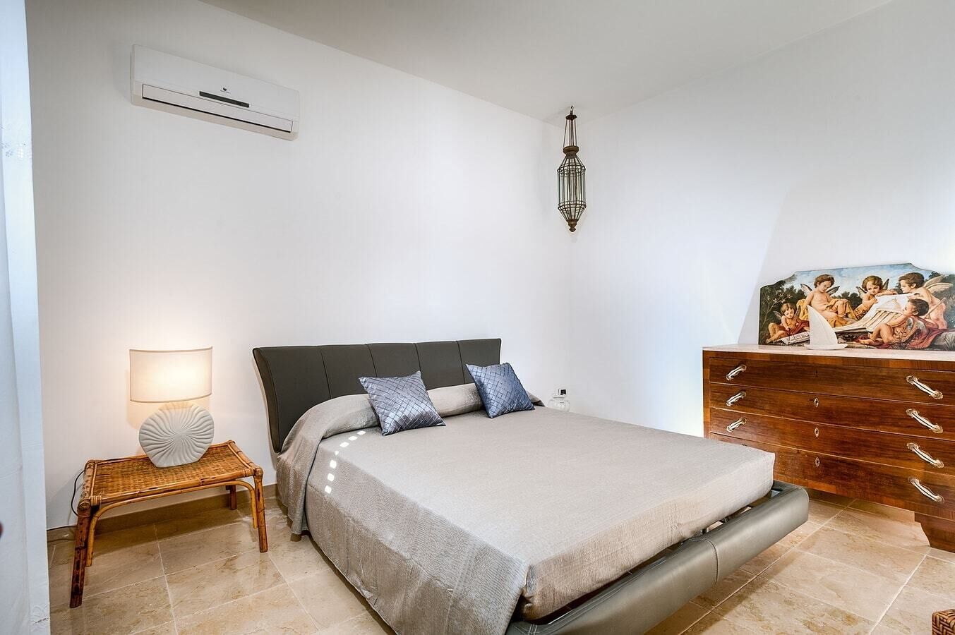 Een slaapkamer met een bed, nachtkastje, lamp, kaptafel en kunstwerk.