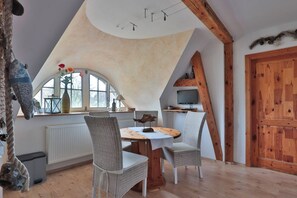 A cozy room with a sloped ceiling, a round dining table, wicker chairs, a wooden door, and a television.