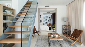 Un salon moderne avec un escalier en verre, une table basse agrémentée d’objets décoratifs et un lit en arrière-plan.