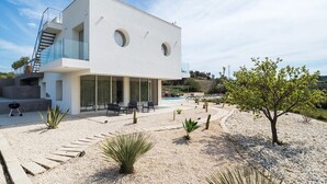 Une maison moderne à deux étages, dotée d’une piscine, d’un espace extérieur aménagé et surplombant un paysage désertique.