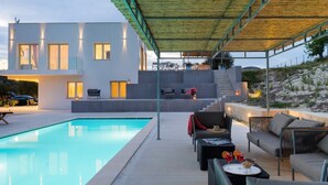 Une maison moderne dotée d’une piscine, d’un espace salon extérieur et d’un patio couvert.