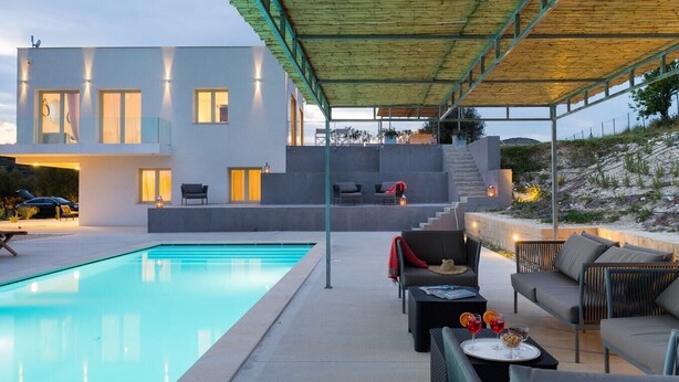 Une maison moderne dotée d’une piscine, d’un espace salon extérieur et d’un patio couvert.
