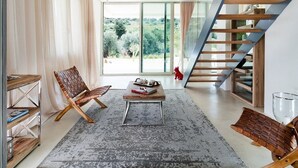 Un salon moderne avec une grande fenêtre, une table basse en bois, un fauteuil en cuir et un escalier.