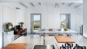 Une cuisine moderne dotée d’un îlot central, d’un coin repas avec une longue table et d’une vue sur l’extérieur grâce à de grandes portes coulissantes.