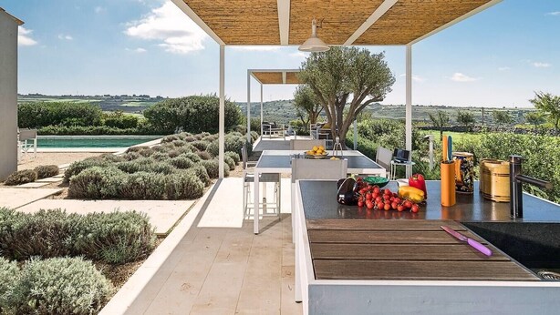 Une terrasse extérieure avec une table dressée pour le repas, entourée d’arbustes soigneusement taillés et offrant une vue sur la campagne.