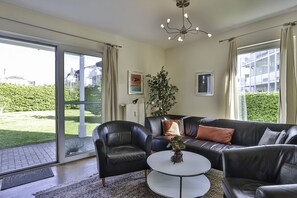 Relax in this stylish living room with a sliding glass door leading to a serene outdoor area, a black leather sofa, and a cozy armchair.