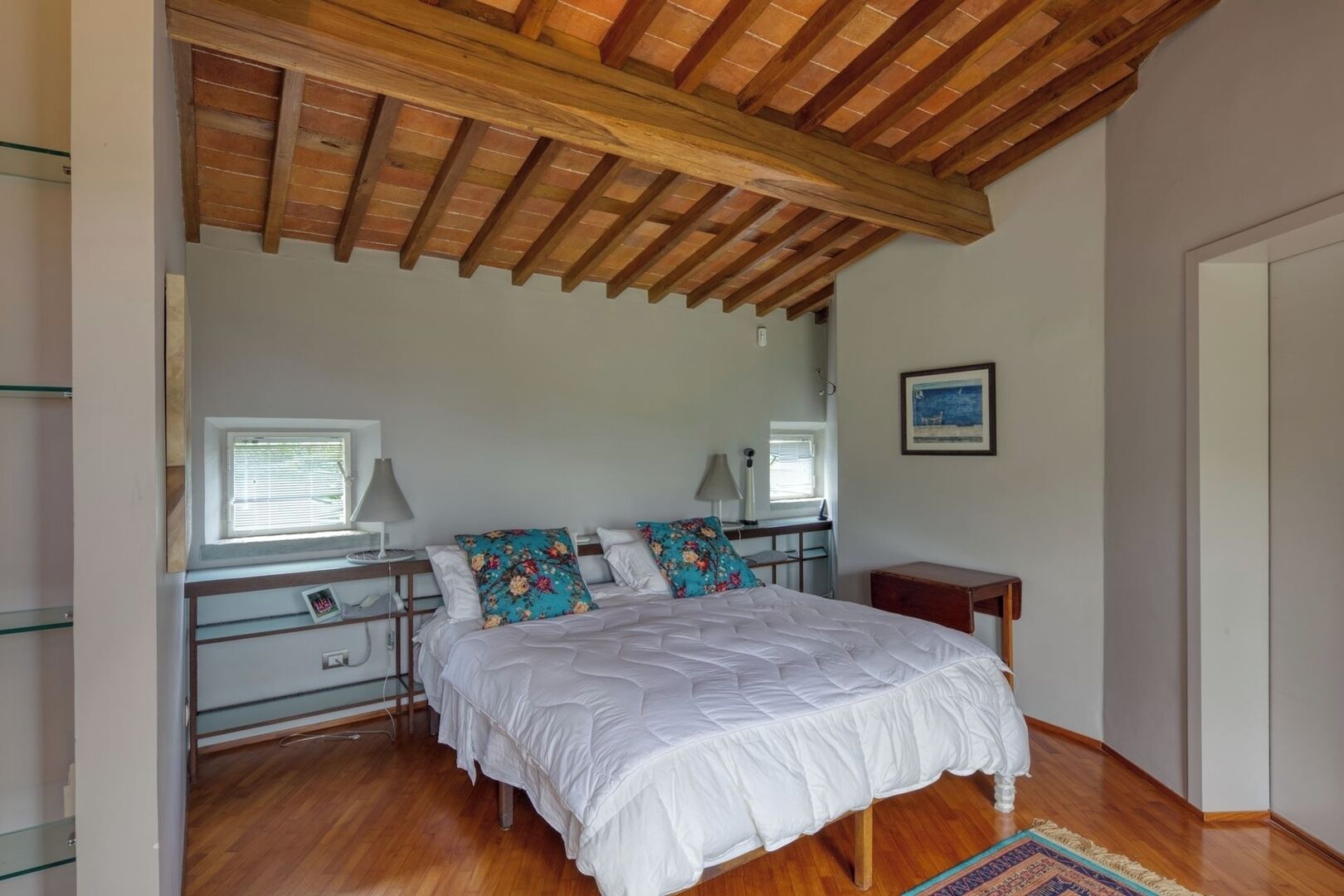 Un dormitorio con techo de madera, una cama con ropa de cama blanca, un escritorio con lámpara y una mesita.