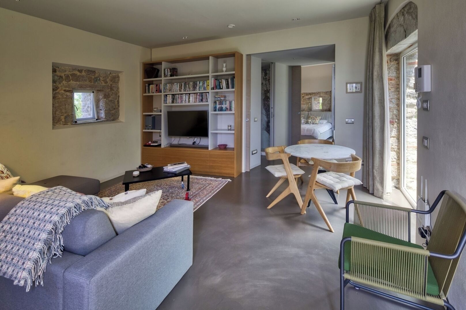 Un salon moderne avec un canapé gris, une table basse, une bibliothèque et un téléviseur. On y trouve également un coin repas avec une table ronde et des chaises.