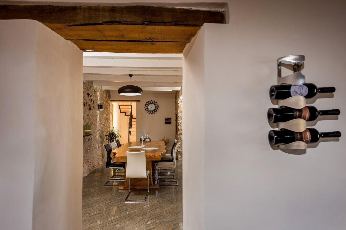 A dining area with a wooden table and chairs, a stone wall, and a clock on the wall.