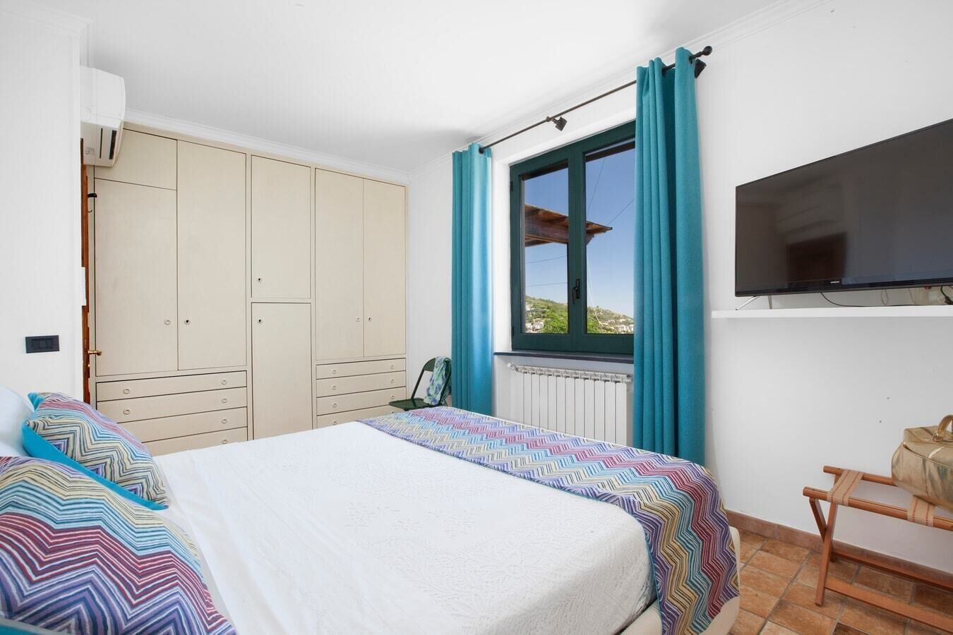Une chambre à coucher avec un lit, une armoire, une télévision et une fenêtre avec des rideaux.