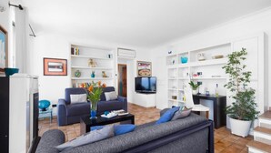 A modern living room with a grey sofa, a blue armchair, and a coffee table. There are white shelves with decorative items and a television. - Villa Carina with sea views (Sant'Agata Sui Due Golfi)