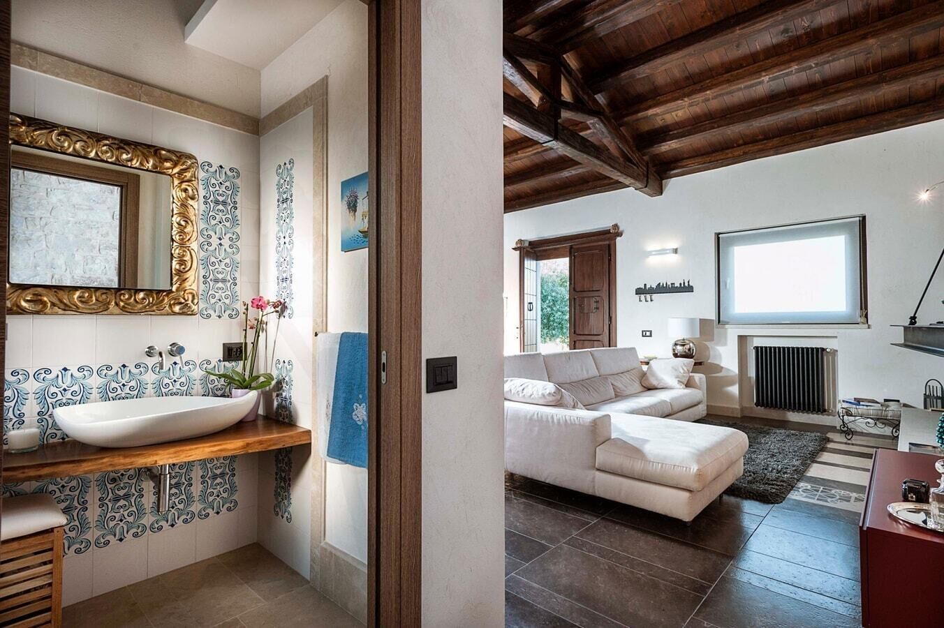 A bathroom with a large sink and a mirror, a living room with a sofa and a radiator.