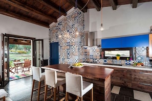 A modern kitchen with a patterned backsplash, wooden bar stools, and a view of the outdoors. - Villa Candia - Private villa with pool near Modica (Rosolini)