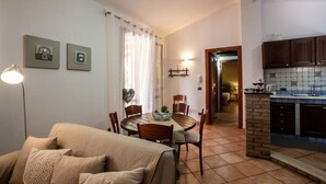 A cozy living room with a sofa, a dining table with chairs, a kitchen area with cabinets and a sink, and a hallway leading to another room. - Villa Colletta + Annex - villa near Scopello (Castellammare del Golfo)