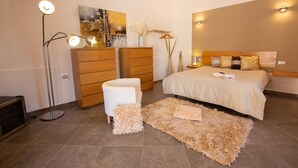 A modern bedroom with a large bed, a dresser, a desk, and a floor lamp. - Villa Colletta + Annex - villa near Scopello (Castellammare del Golfo)