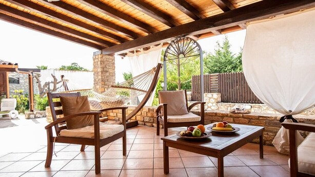 An outdoor patio with wooden furniture, a hammock, and a table with fruit. - Villa Colletta + Annex - villa near Scopello (Castellammare del Golfo)