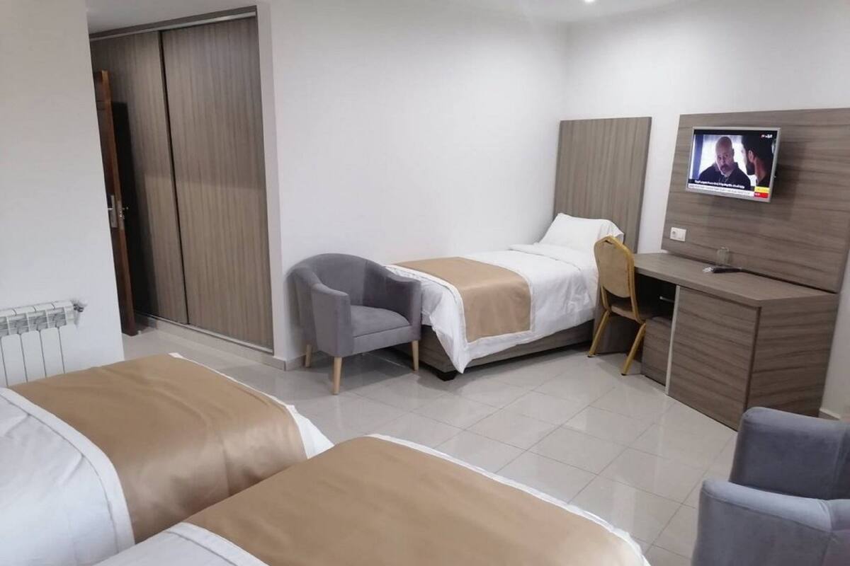 Ein Hotelzimmer mit zwei Betten, einem Schreibtisch, einem Sessel und einem Fernseher.
