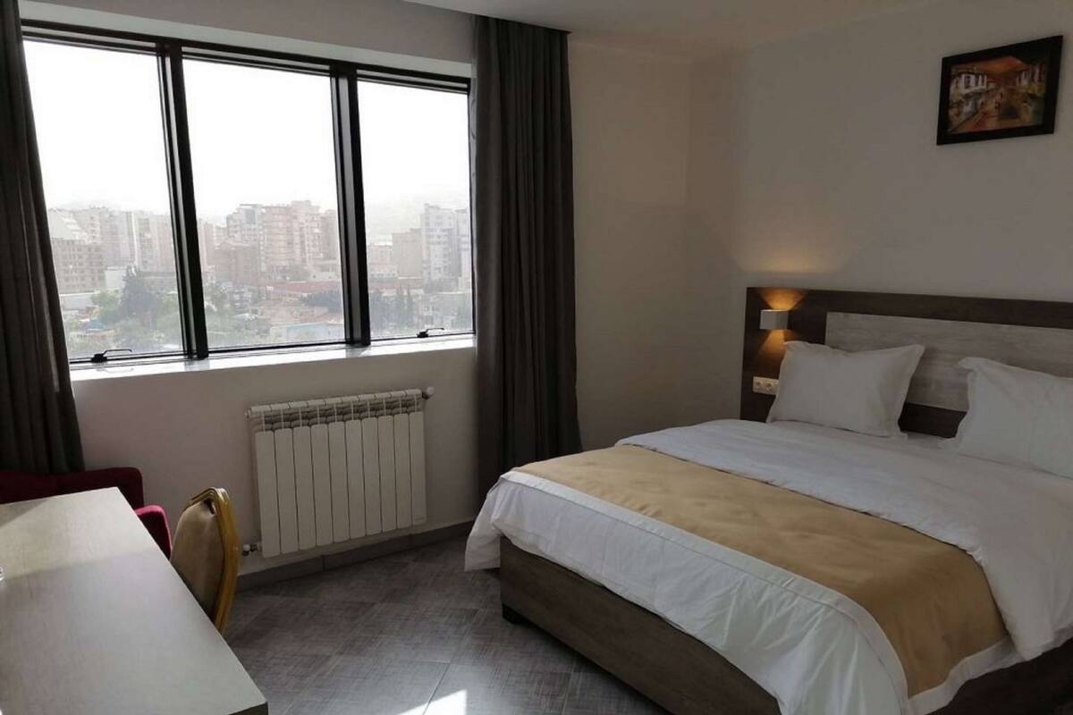 Ein Hotelzimmer mit Bett, Schreibtisch, Fenster mit Blick auf die Stadt und Heizkörper.