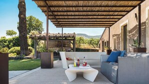 An outdoor patio with a covered seating area, a table with bottles, and a view of a vineyard in the background. - Villa Etnea - Private villa with pool and jacuzzi (Zafferana Etnea)