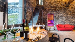 Interior de paredes de piedra con una zona de bar, copas de vino, botellas y un sofá rojo.