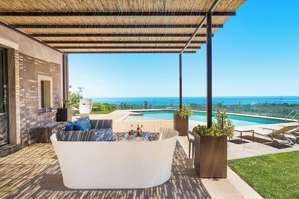 A covered outdoor area with a pool, a white sofa, and lounge chairs.