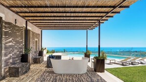 Un área exterior moderna con una bañera grande, asientos y vistas al océano.