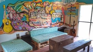 Una habitación con un mural colorido, un banco de madera, una mesita y una guitarra.