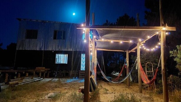 Un espacio al aire libre rústico con una estructura de madera, luces colgantes y una hamaca.