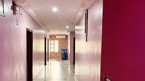 Un couloir avec un sol à carreaux, des murs roses et une porte rouge sur le côté droit.
