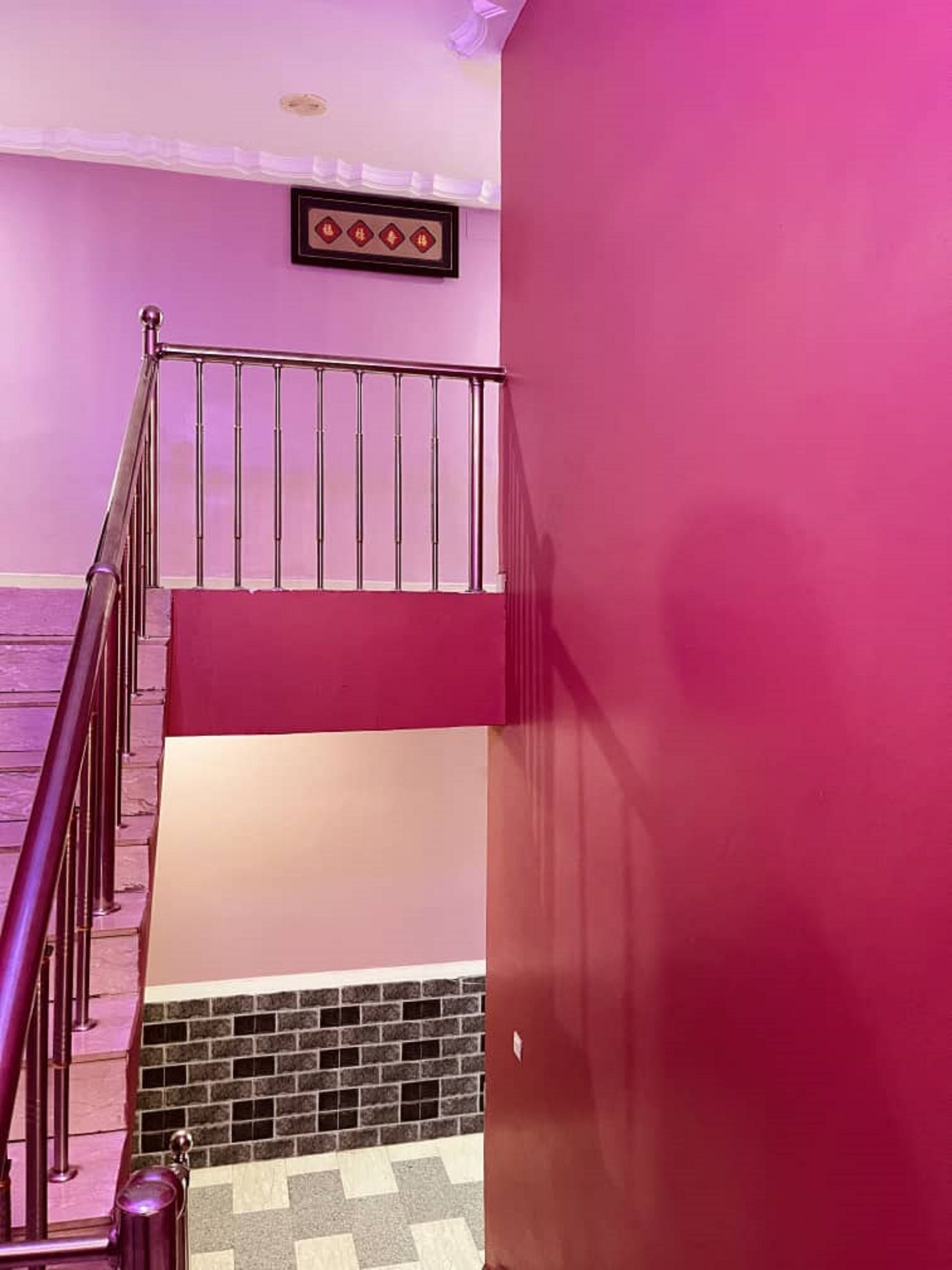 Una escalera con barandilla de metal, pared rosa y suelo de baldosas.