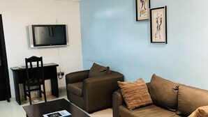 Un salon avec un canapé marron, une table basse, un téléviseur et des œuvres d’art encadrées accrochées au mur.