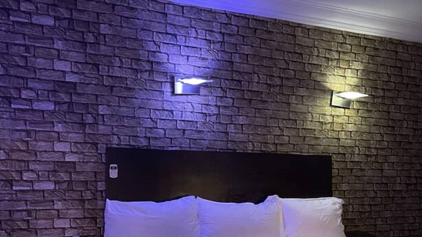 Une chambre avec un mur décoré d’un motif en briques, une tête de lit en bois et deux lampes de chevet.