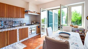 A modern kitchen with wooden cabinets, a tiled backsplash, and a dining area with a table and chairs. - Villa Gesine with private pool and sea views (Massa Lubrense)