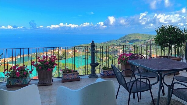 A terrace with a table and chairs, potted plants, and a view of the sea and landscape. - Villa Gesine with private pool and sea views (Massa Lubrense)