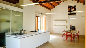 A modern kitchen with a white island, red chairs, and a dining table set for four. - Villa Garofano - Coastal villa with pool (Marsala)