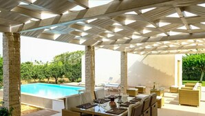 A covered outdoor area with a pool, wicker furniture, and a view of greenery. - Villa Garofano - Coastal villa with pool (Marsala)