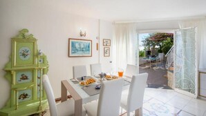 Een eethoek met een tafel voor twee personen, een groene kast met bloemmotieven en uitzicht op een terras.