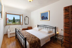 A bedroom with a bed, a nightstand, a lamp, a mirror, and a window with a view of greenery and buildings. - Villa Vesna - Private Villa with pool, Brac Island (Sumartin)