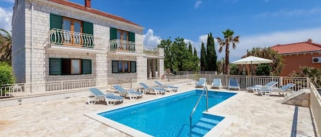 A two-story building with a swimming pool, lounge chairs, and a tiled patio.