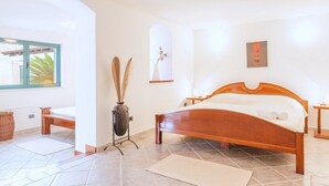 A bedroom with a wooden bed, a small bedside table, a vase with dried plants, and a window with a view of palm trees. - Villa Venera - Coastal Villa with pool in Sumartin (Sumartin)