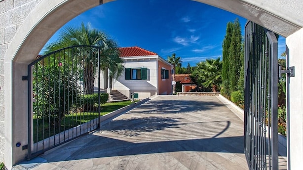 A pathway leading to a house with a red-tiled roof, surrounded by greenery and palm trees. - Villa Venera - Coastal Villa with pool in Sumartin (Sumartin)