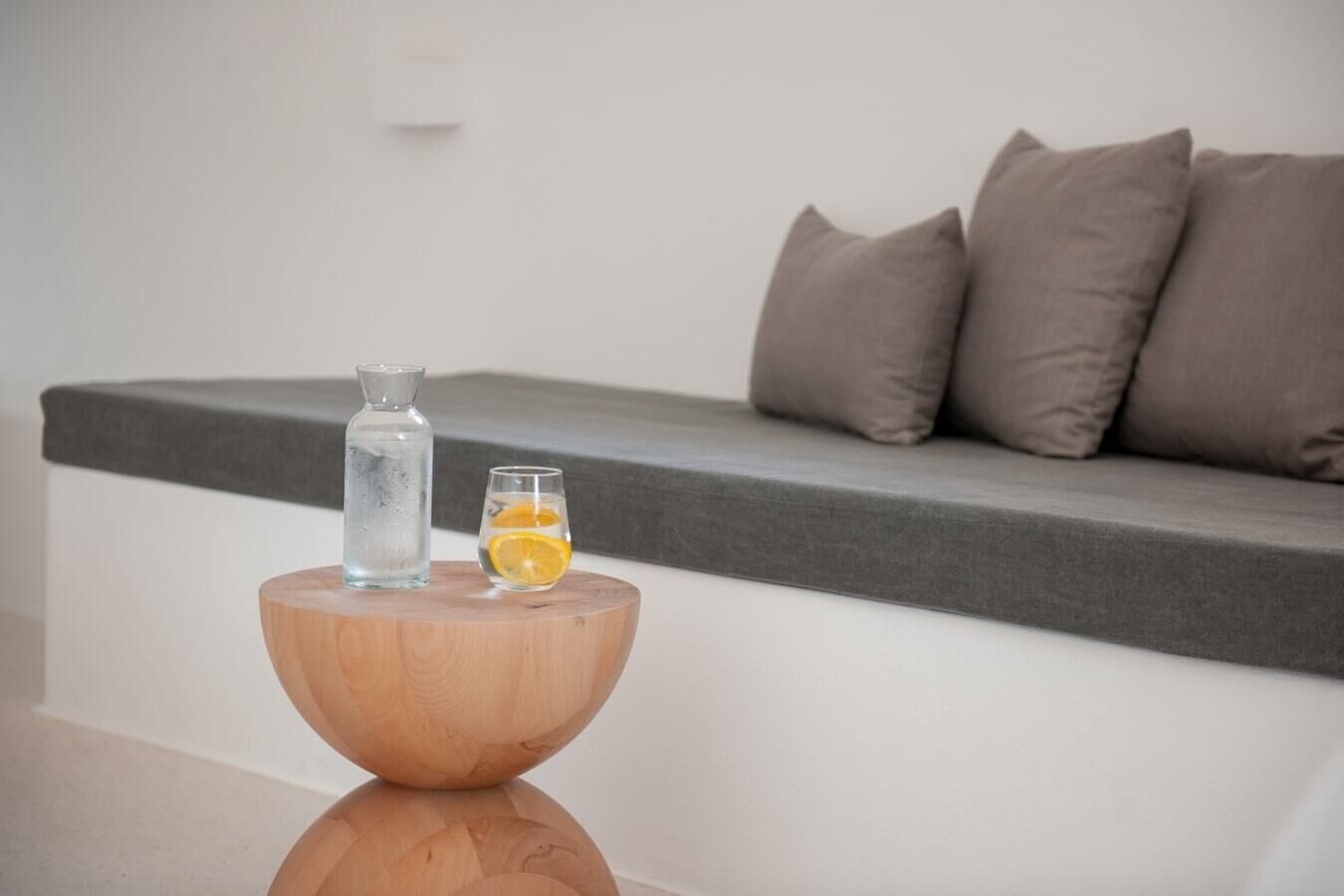 A wooden side table with a clear glass bottle and a glass containing an orange slice.