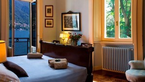 A hotel room with a bed, a window with a view of the sea, a radiator, and a chair. - Villa Vanessa - Luxurious waterfront private villa (Moltrasio)