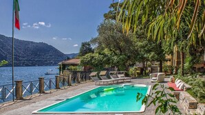 A pool area with a view of a lake and mountains, surrounded by greenery and a flag. - Villa Vanessa - Luxurious waterfront private villa (Moltrasio)