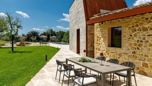 A modern outdoor dining area with a stone building, a pool, and a well-maintained lawn.