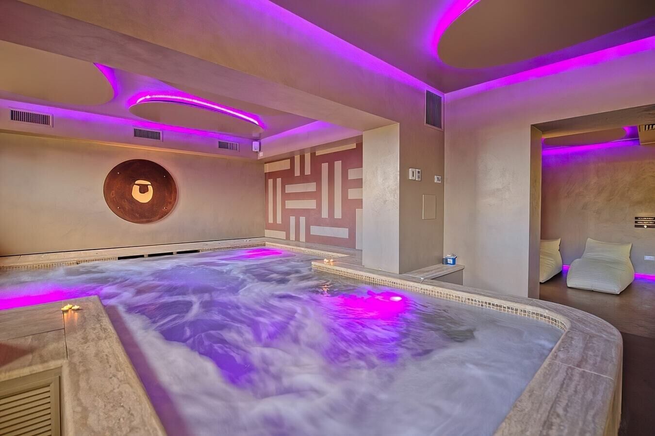 Une salle de spa dotée d’un jacuzzi, d’un éclairage d’ambiance violet et d’un design moderne.